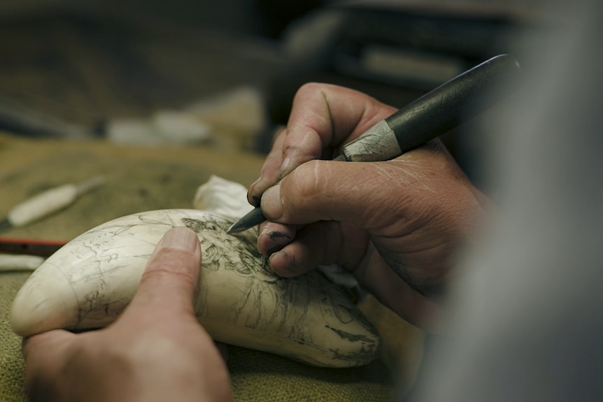 closeup of hands using scribe to engrave large whale tooth
