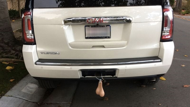 A white suv with fake scrotum hanging from the tow bar