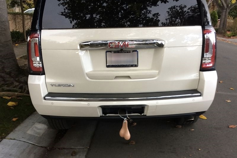 A white suv with fake scrotum hanging from the tow bar