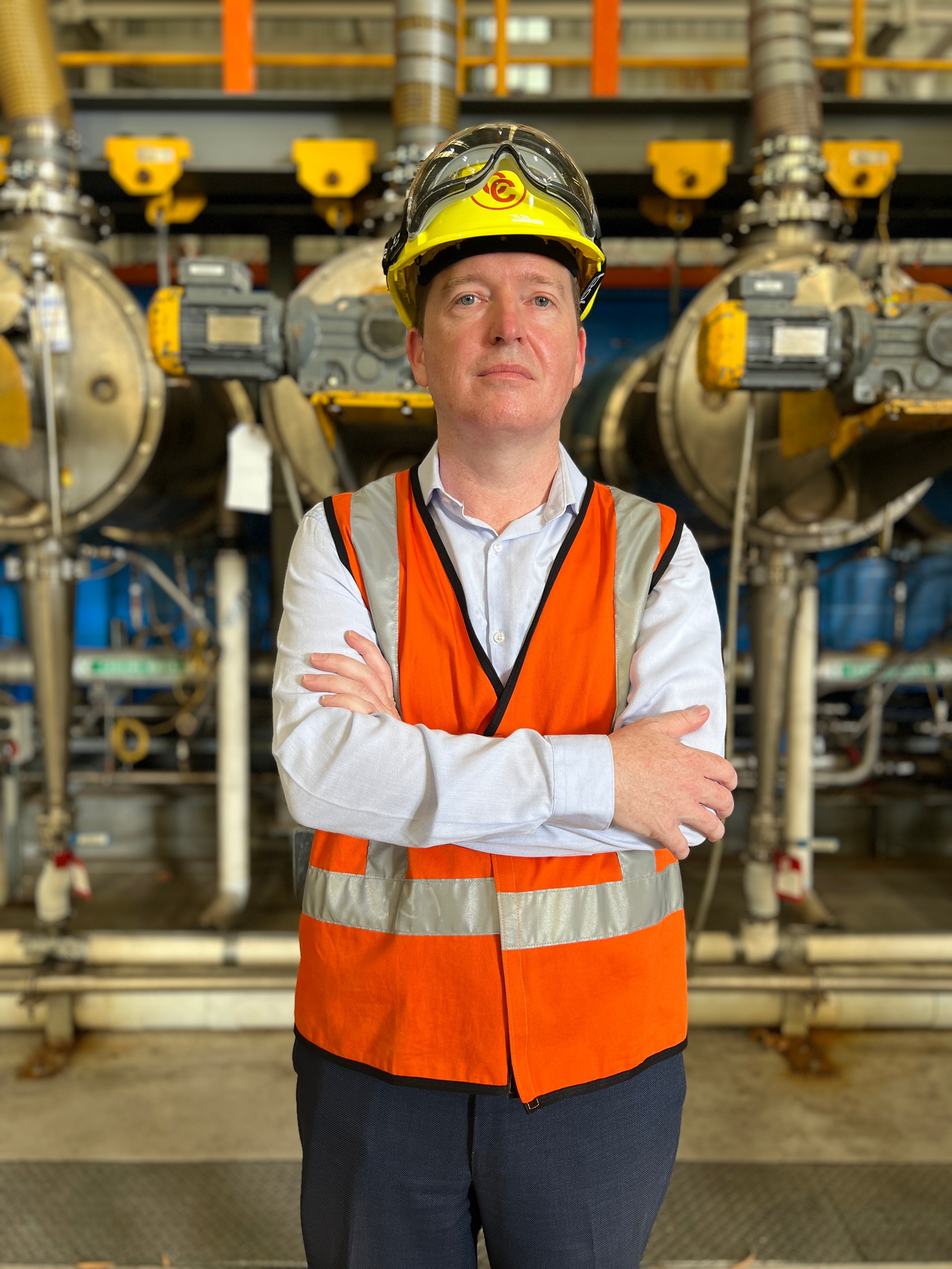 A man wearing a high-vis vest and hard hat looks straight at the camera. 