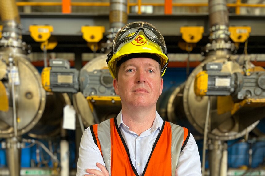 A man wearing a high-vis vest and hard hat looks straight at the camera. 