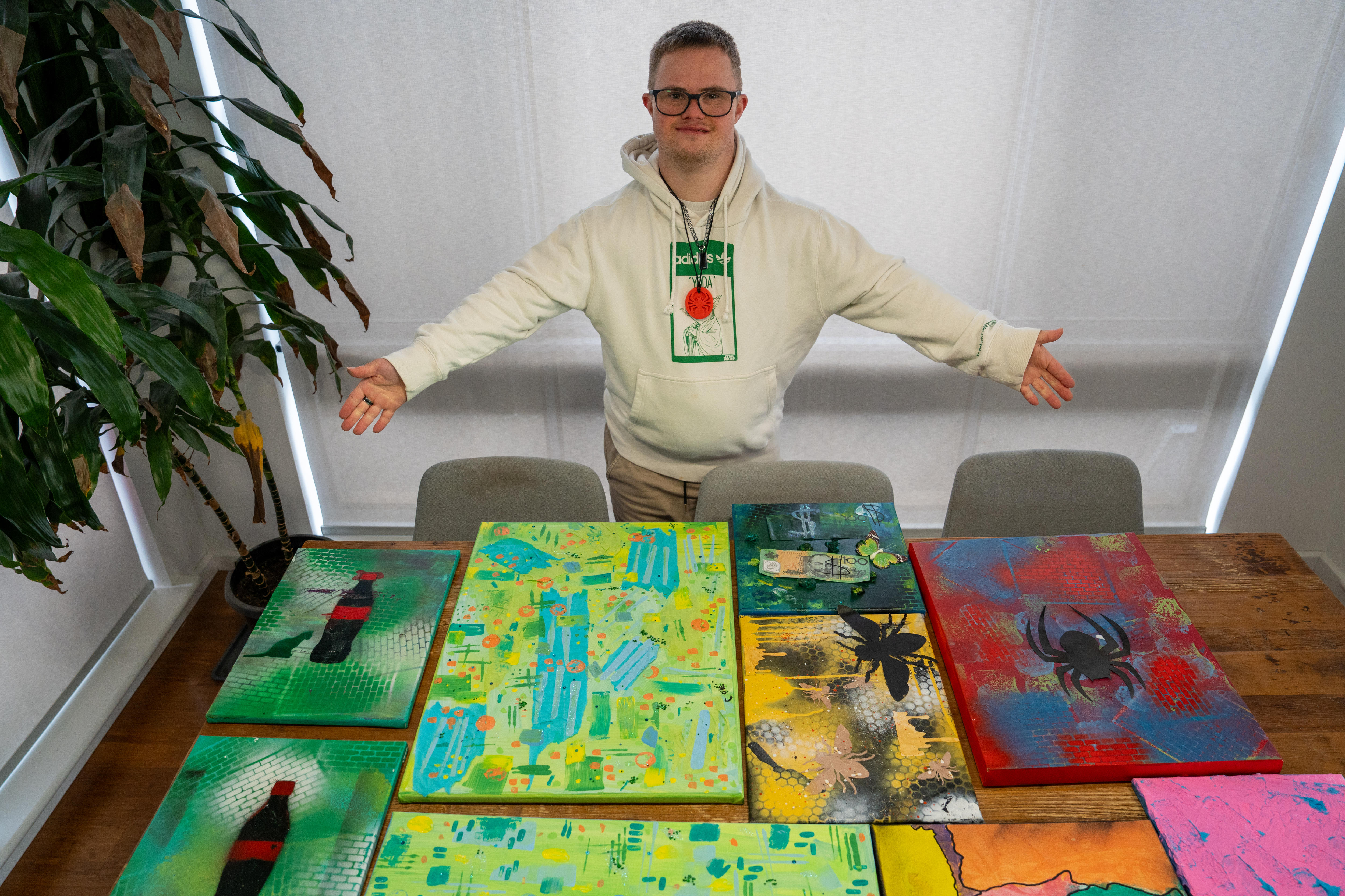 Artist stands over table of his artwork, motioning at them with his hands