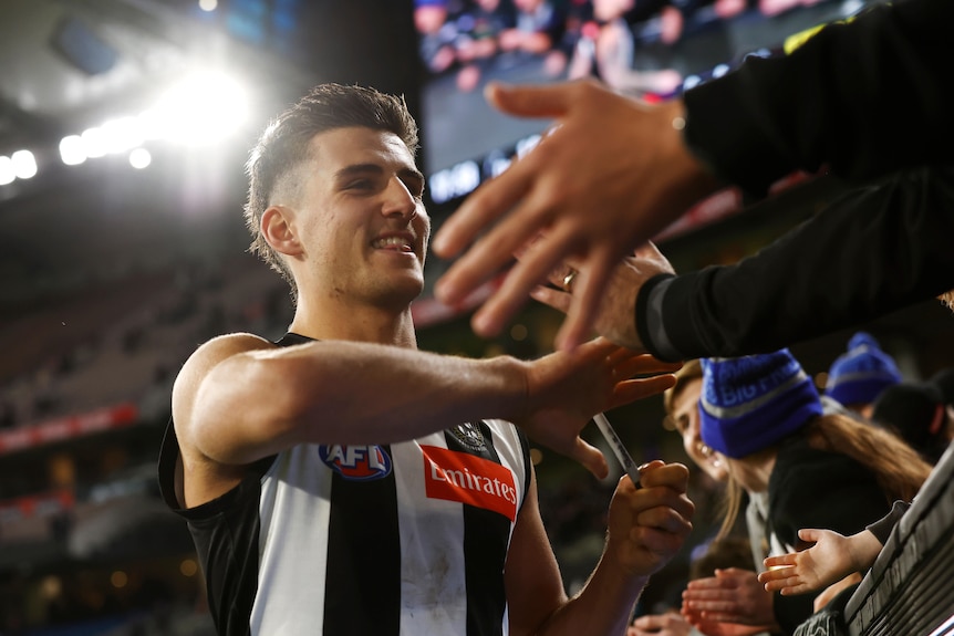 Nick Daicos smiles while high-fiving Collingwood fans over the fence