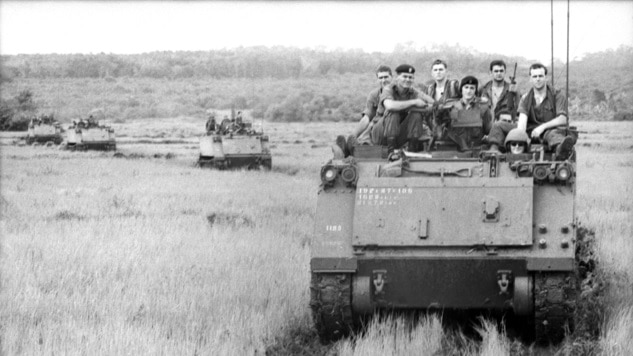 Soldiers in a tank driving through grass