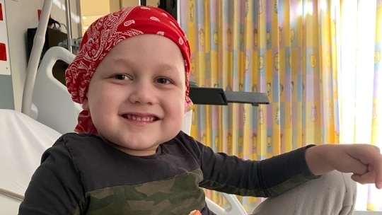 A young boy smiles wearing a hard scarf eating fruit.