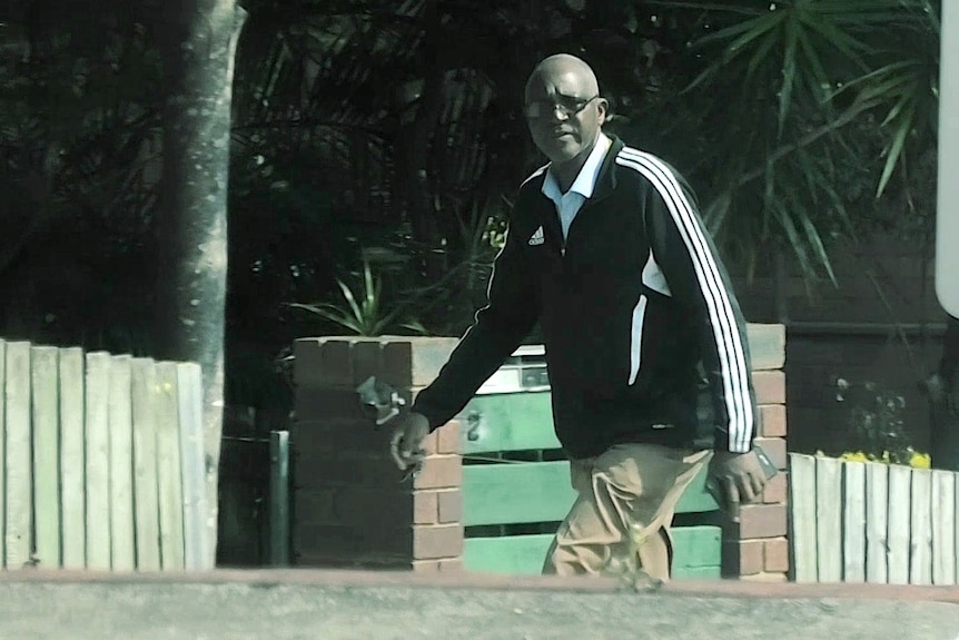 A man in a tracksuit top and glasses walking in a residential street