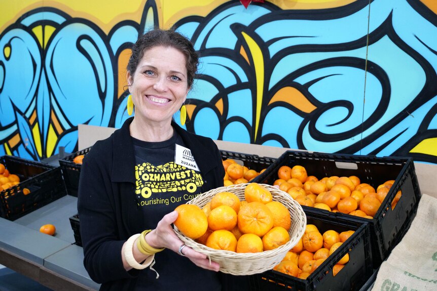 A woman smiles as she holds a basket of oranges.