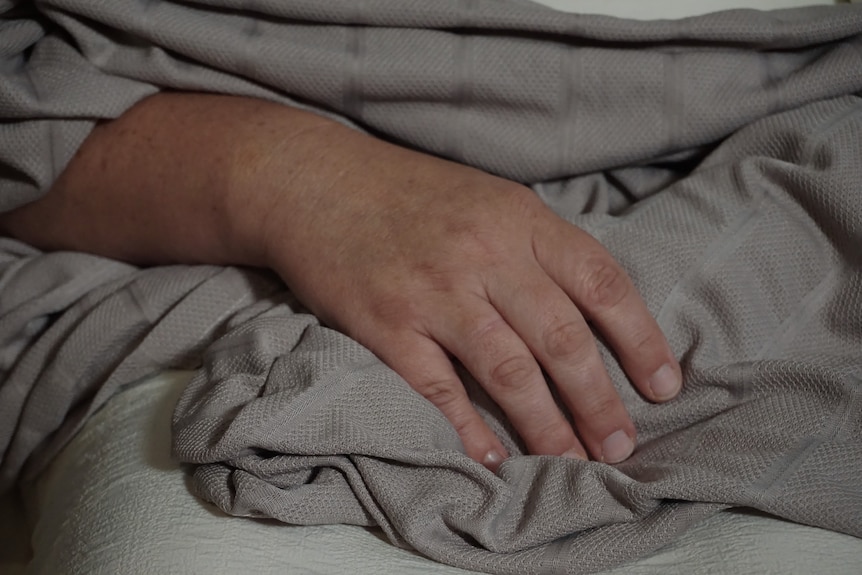 A woman's hand rests on a grey blanket.