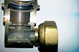 A close-up of a small brass inlet elbow connector which has been cut in half to show internal corrosion.
