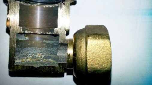 A close-up of a small brass inlet elbow connector which has been cut in half to show internal corrosion.