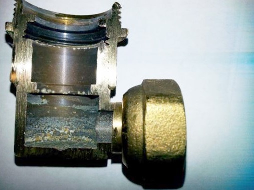 A close-up of a small brass inlet elbow connector which has been cut in half to show internal corrosion.