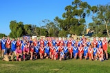 Group of women dressed in footy jersey, shorts, coloured in red and blue with a white V down the front pose on a football field.