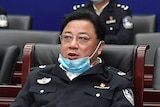 a man with a mask on his chin in a uniform sits in a chair at a meeting