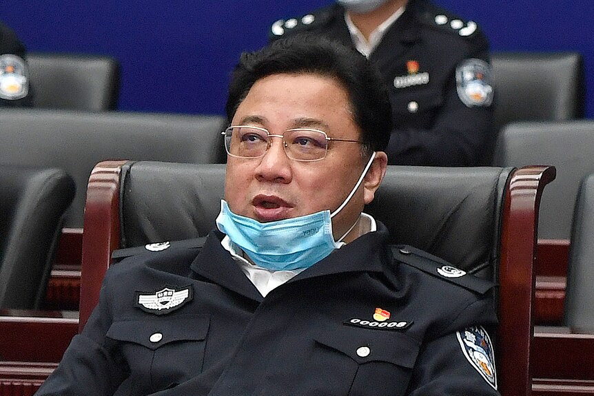 a man with a mask on his chin in a uniform sits in a chair at a meeting