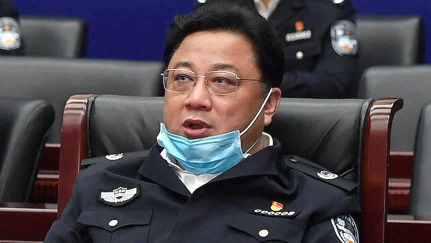 a man with a mask on his chin in a uniform sits in a chair at a meeting