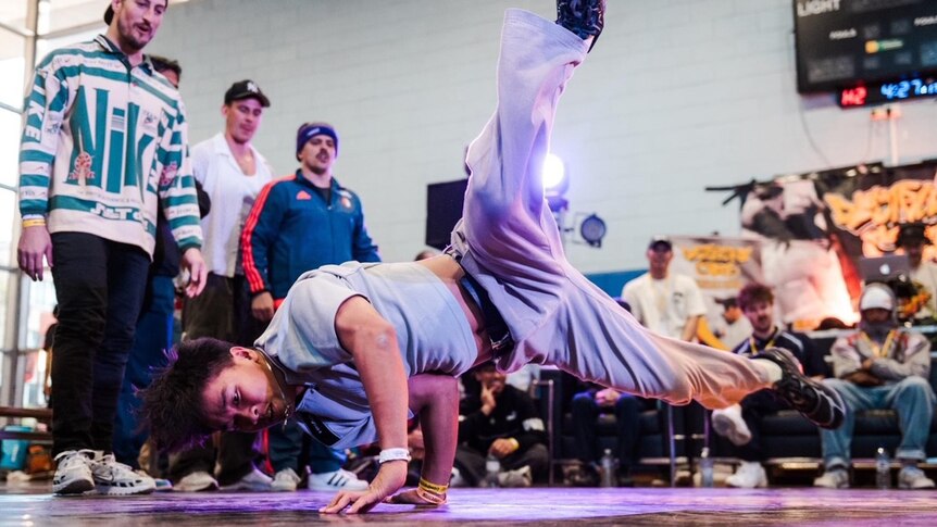Jeff does a handstand during a competition, spectators watch from the edge of the dance floor.