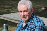 elderly man sitting at a table with thermoflask, smiling.