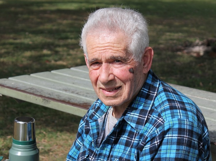 elderly man sitting at a table with thermoflask, smiling.