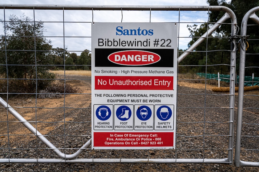 A sign that reads "Santos Bibblewindi #22 No Unauthorised Entry" sits on a padlocked gate in a forest.