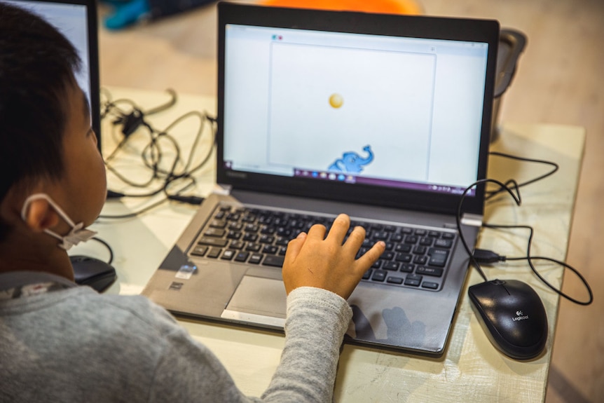 A generic photo of a child using a laptop in class, with a cartoon elephant on screen.