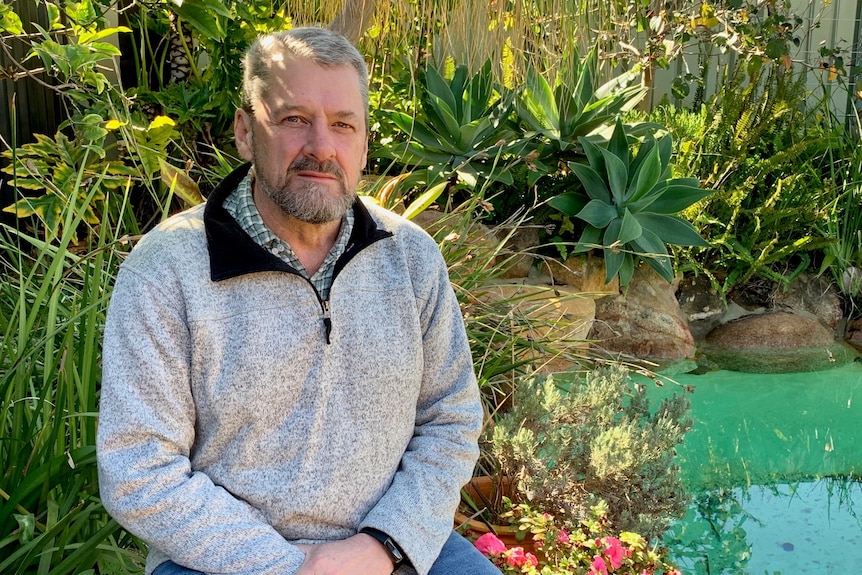 A middle aged man sitting outside in a garden near a pond