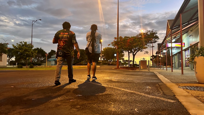 A man and a woman walk down the street with sunset in the background.