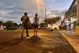 A man and a woman walk down the street with sunset in the background.