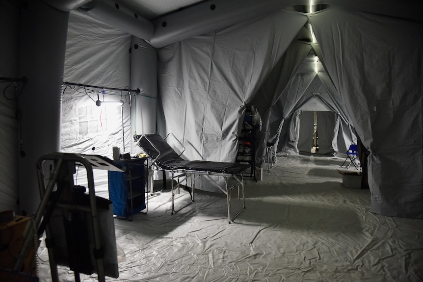 An interior view of a field hospital, with a simple hospital bed and curtain partitions betwen areas.