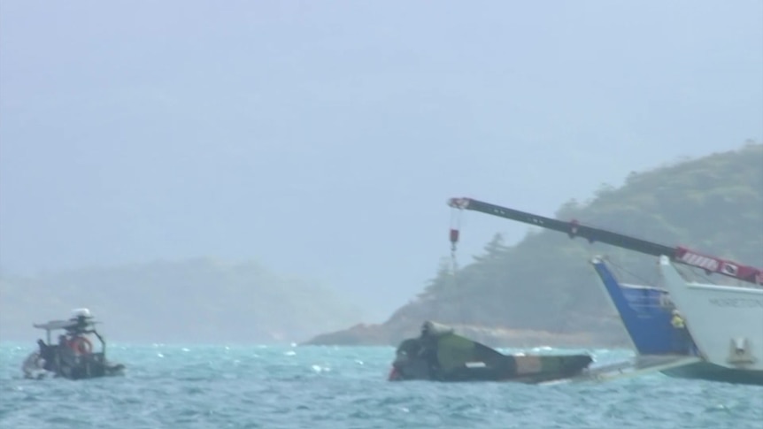 A ship pulls Taipan wreckage from the ocean, authorities are in a smaller watercraft nearby