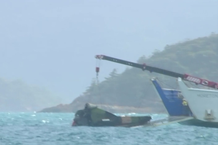 A ship pulls Taipan wreckage from the ocean, authorities are in a smaller watercraft nearby
