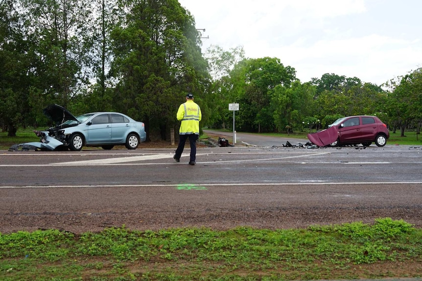 a police officer is seen walking across the road toward a blue car and a red car smashed after bring in a crash.