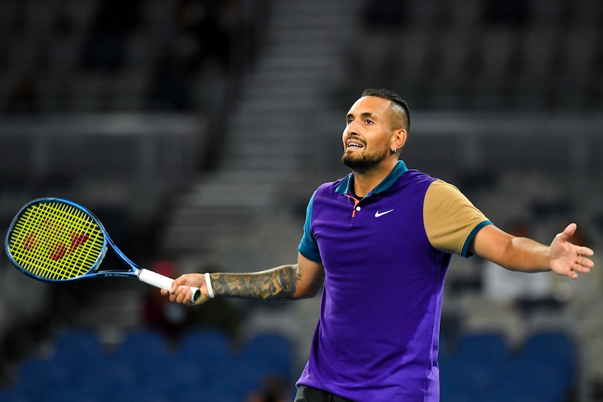 Nick Kyrgios holds his arms out and smiles while looking up towards the crowd