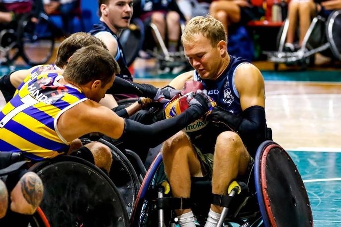 Wheelchair rugby players grapple for a ball.