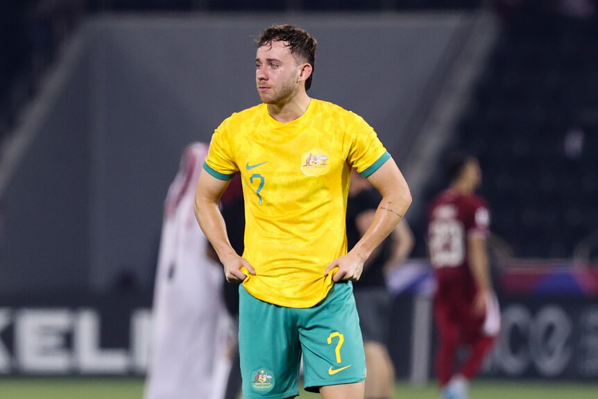 Olyroos player Lachlan Brook stands with his hands on his hips, crying after losing a soccer game.