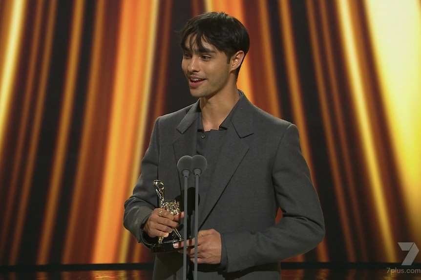 A man wearing a suit accepting an award on stage 