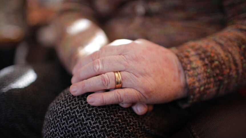 An older woman's hands folded in her lap, with wedding rings.