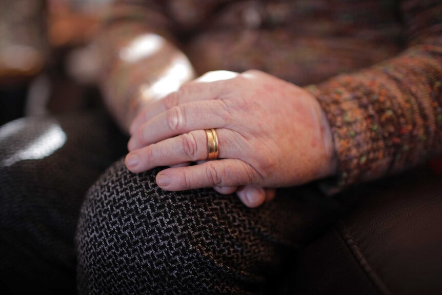 An older woman's hands folded in her lap, with wedding rings.