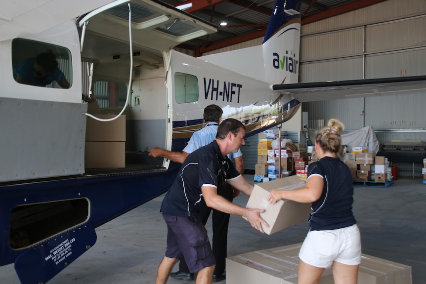 three people loading small plane with boxes 