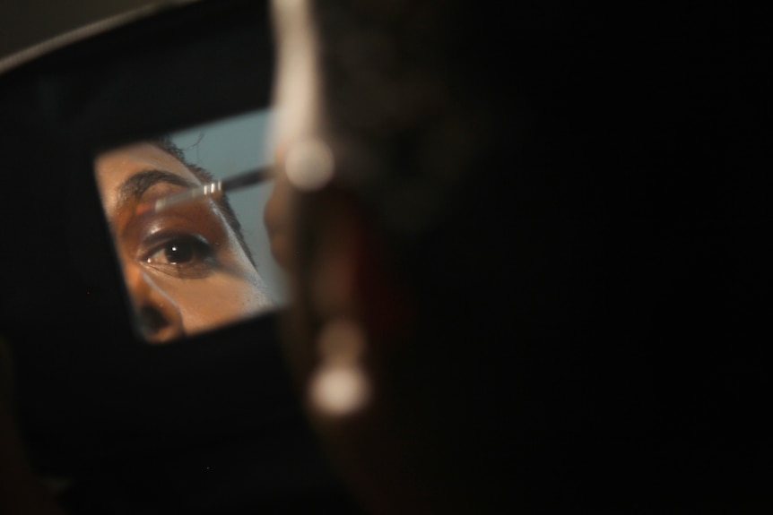 A photo of Shaniqua's reflection in a small mirror as she applies eyeliner.