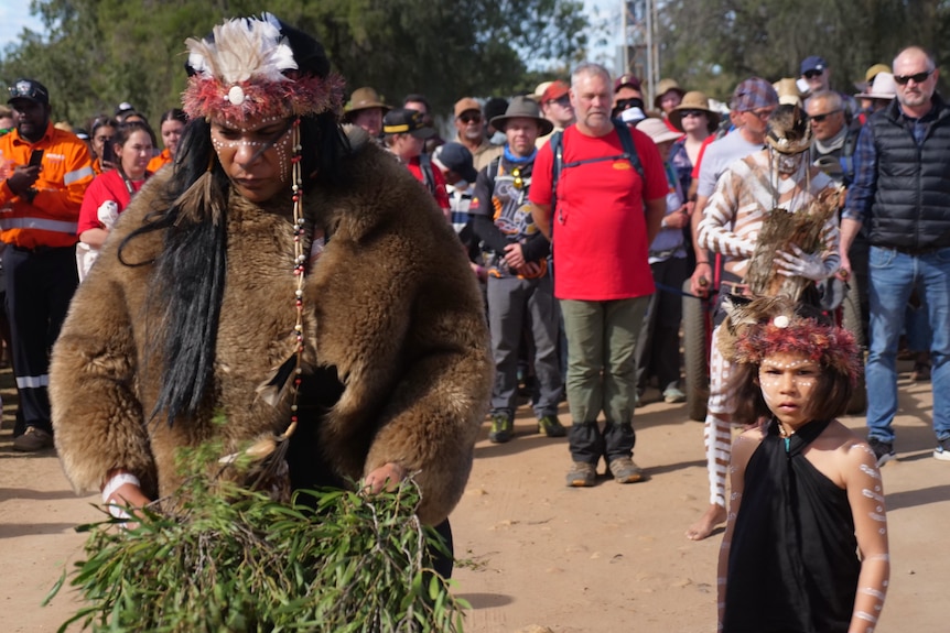 A woman and a girl wear headdresses in front of a crowd.