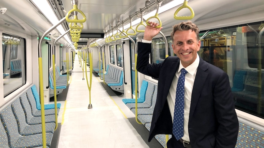 A man in a blue suit holds a handrail on a new train that has wrapping on its floor.