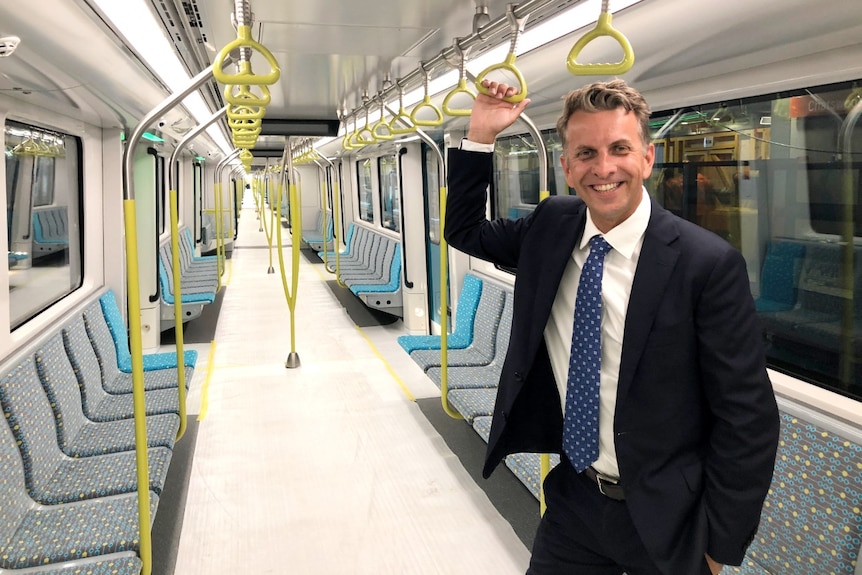 A man in a blue suit holds a handrail on a new train that has wrapping on its floor.