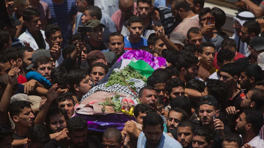 A group of mourners are seen carrying a body covered by the Palestinian flag and flower in a funeral procession.