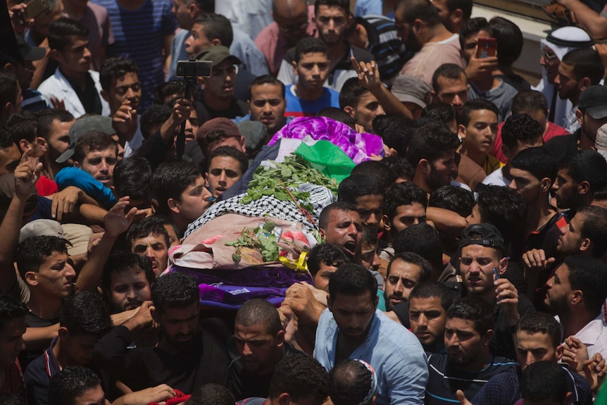 A group of mourners are seen carrying a body covered by the Palestinian flag and flower in a funeral procession.