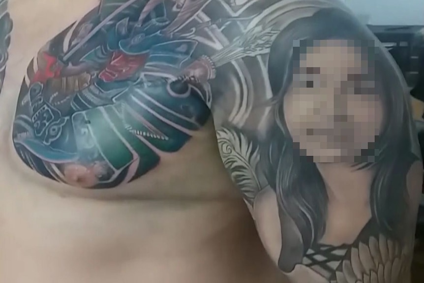 An man's arm and chest is seen covered in colourful tattoos including the blurred face of a woman.