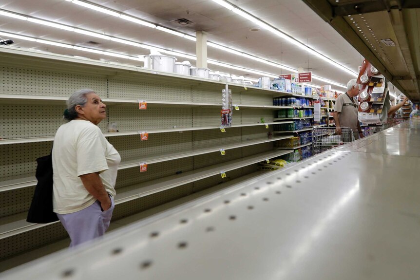 A shopper walks past an empty supermarket shelf .