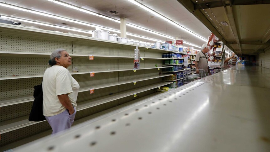 A shopper walks past an empty supermarket shelf .