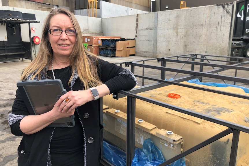 A woman stands next to a car battery. 