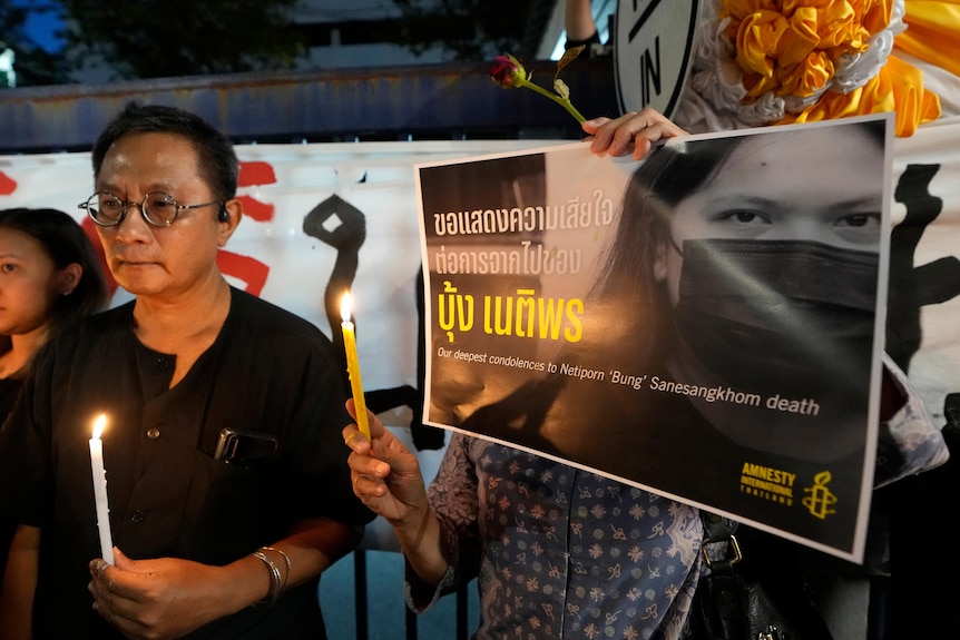 A man holds a lit candle next to a woman holding a poster and a candle