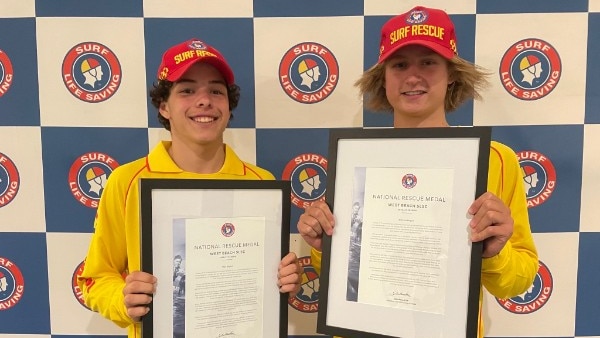 Two boys dressed in yellow and red life saving uniforms holding a framed award